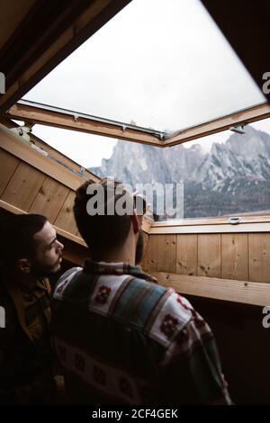 Dal basso, vista sul retro di uomini viaggiatori in abbigliamento casual Ammirate il paesaggio delle montagne dolomitiche in Italia dal cielo Foto Stock