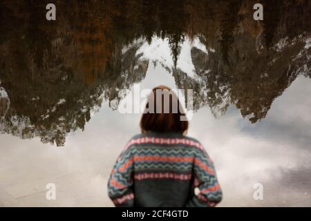 Vista posteriore di anonimo viaggiatore donna in abbigliamento casual in piedi e deliziare in vista del lago con le montagne delle Dolomiti nebbia sullo sfondo in Italia Foto Stock