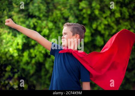 Supereroe ragazzo bambino contro sfondo verde all'aperto. Infanzia, successo e concetto di potere Foto Stock