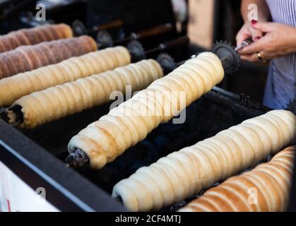 Cottura tradizionale di pasta vecchia Boemia trdelnik - spiedo dolce pasta di pasta arrotolata avvolta intorno bastone e grigliata Foto Stock