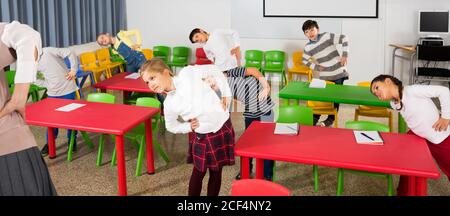 Ritratto di bambini lo stiro con gentile maestro femmina durante l'attività fisica break nella scuola Foto Stock