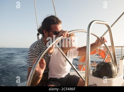 Padre e figlio galleggiano su barca costosa sul mare e. cielo blu in giornata di sole Foto Stock