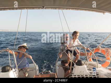 Felice padre con i bambini che galleggiano su barca costosa sul mare e cielo blu in giornata di sole Foto Stock
