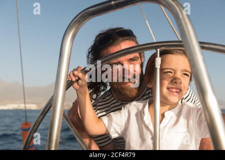 Felice padre con i bambini che galleggiano su barca costosa sul mare e cielo blu in giornata di sole Foto Stock