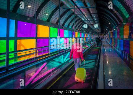 donna anonima con passerella di falciatura in valigia vicino a pannelli colorati All'interno dell'aeroporto Barajas di Madrid in Spagna Foto Stock