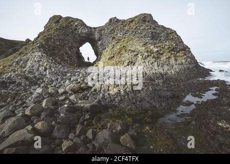 Vista laterale di femmina in abiti caldi in piedi sulla scogliera Bordo all'interno della grotta nel porto dell'Irlanda del Nord guardando lontano in mare Foto Stock