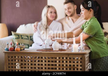 donna thailandese che versa il tè per una coppia nella sala spa Foto Stock