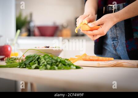 anonimo Donna taglio carote mentre cucinando insalata sana in cucina Foto Stock