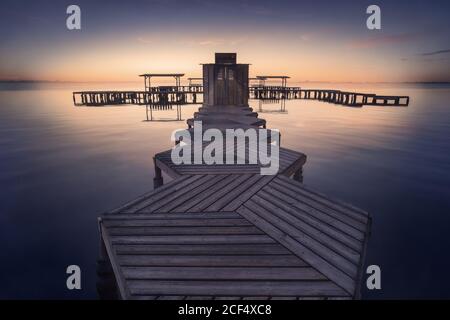 Vista aerea del molo geometrico in legno vuoto sopra l'acqua tranquilla su luminoso sfondo tramonto Foto Stock