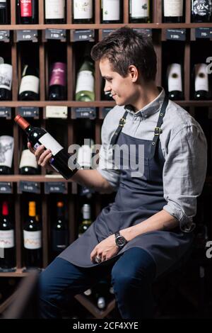 Sommelier maschile concentrato in suite guardando il vino rosso in bottiglia Foto Stock