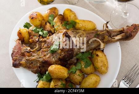 Agnello al forno gamba servito con patate e prezzemolo delizioso agnello al forno servito gamba intera con patate al forno e guarnite con prezzemolo appetitoso Foto Stock