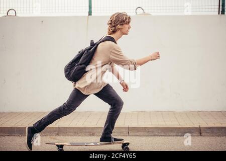 Giovani ricci capelli lunghi uomo a cavallo su longboard sulla strada vuota Foto Stock