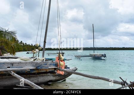 Piccole barche da pesca in legno lungo una spiaggia tropicale sull'Isola di Pines, Nuova Caledonia. Una barca è stata messa a terra sulla sabbia mentre altre sono ancorate. Foto Stock