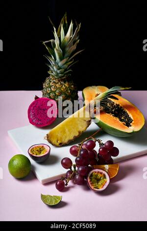 Ancora vita con frutti tropicali: Papaia a fette, ananas, pitaya e uva su taglio marmo Foto Stock