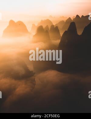Sagome di grandi montagne alte contro il cielo nuvoloso luminoso sopra Mattina nebbia a Guilin Foto Stock