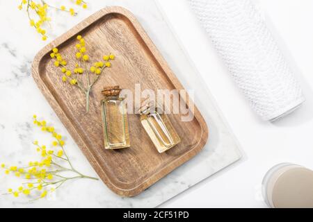 Vista dall'alto del fiore mimosa e del suo essenziale olio su vassoio di legno su tavolo di marmo Foto Stock