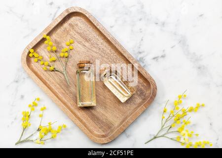 Vista dall'alto del fiore mimosa e del suo essenziale olio su vassoio di legno su tavolo di marmo Foto Stock