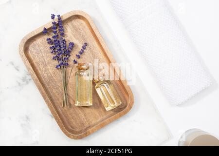 Vista dall'alto fiore di lavanda e il suo olio essenziale su un bottiglia su un tavolo di marmo su un vassoio di legno Foto Stock