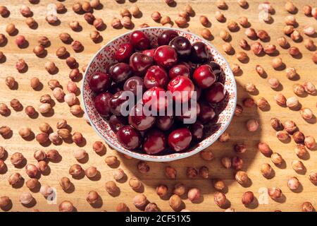 Vista dall'alto delle ciliegie dolci fresche in ciotola con ciliegia semi intorno su tavola di legno Foto Stock