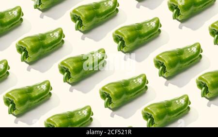 Da sopra composizione creativa di pepe verde intero a fette sopra superficie bianca Foto Stock