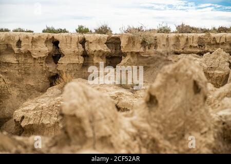 Rocce secche grandi con vegetazione verde sparse sotto il cielo blu e nuvole bianche in Bardenas Reales, Navarra, Spagna Foto Stock