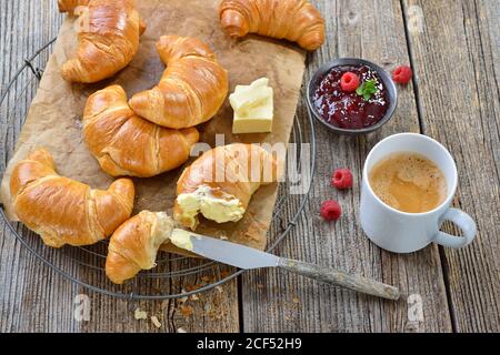 Colazione con croissant appena sfornati su una griglia, servita con burro, marmellata e una tazza di crema di caffè Foto Stock