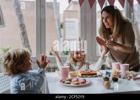 Madre positiva che gioca con i capretti mentre ha partito domestico di compleanno Foto Stock