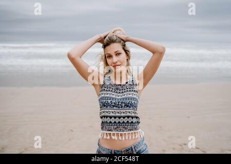 Allegro bionda Donna in top colorato e Jean pantaloncini in posa mentre si rilassa in riva al mare Foto Stock