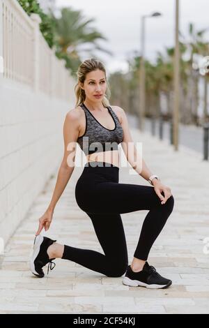 Contenuto giovane atleta in elegante outfit sportivo che si appoggia alle mani in ginocchio durante l'allenamento Foto Stock