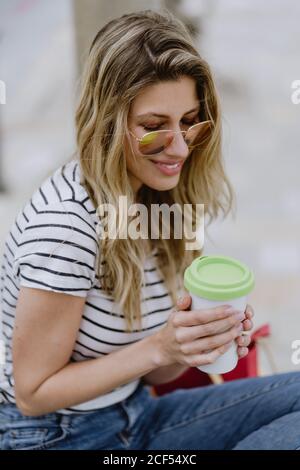 Dall'alto si può vedere la giovane donna allegra e casual da asporto una tazza di caffè seduto sulla panchina della città sul lungomare giorno d'estate Foto Stock