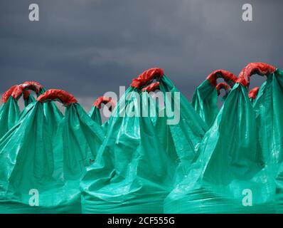 Maniglie in plastica arancione su grandi sacchi verdi blu di fertilizzante agricolo contrastano con cieli oscuri minacciosi su terreni agricoli in Cumbria, Inghilterra, Regno Unito Foto Stock