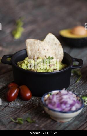 Vista dall'alto di vari ingredienti freschi posti sul tavolo da legno vicino pentola con guacamole yummy Foto Stock