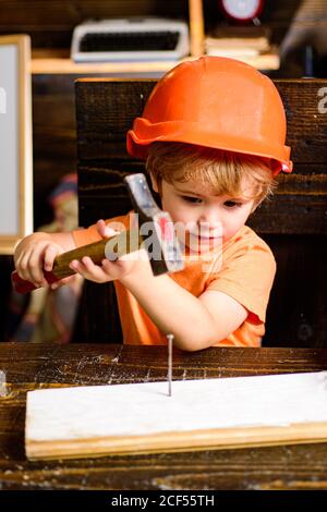 Bambino con casco in elmetto arancione. Costruzione di utensili. Ragazzo martellando. Chiodo martelli bambini. Foto Stock