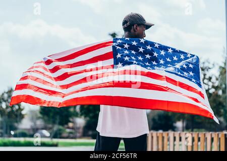 Serio uomo afroamericano che tiene la bandiera americana sulla spalla e. guardando via Foto Stock