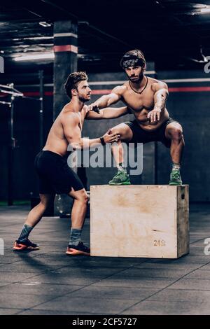 Allenatore atletico saltando sulla scatola e aiutando il cliente a migliorare stamina in palestra Foto Stock