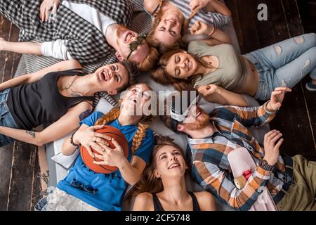 felice gruppo di donne e uomini volti in cerchio ridendo e divertendosi vista dall'alto, sdraiato su coperta, gioiosa celebrazione dei momenti Foto Stock