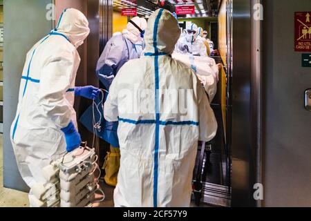 Gruppo di medici irriconoscibili che indossano l'uniforme protettiva mentre prendono il paziente con virus da ascensore in ospedale Foto Stock