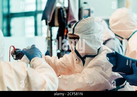Gruppo di medici professionisti che indossano maschere protettive e tute in piedi vicino al tavolo operatorio con attrezzatura e preparazione per il funzionamento in clinica moderna Foto Stock