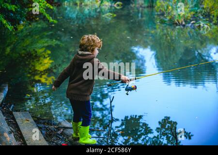 Carino bambino ragazzo tirando canna mentre pesca sul lago. Foto Stock