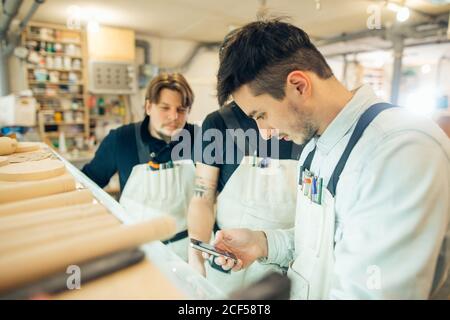 falegname che testava qualcuno sul suo smartphone in un ambiente polveroso officina Foto Stock