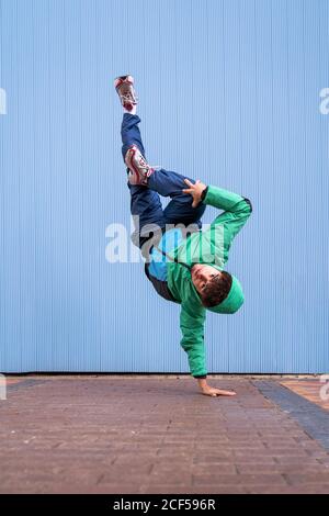 Cool ballerino riccia maschile in abbigliamento sportivo e sneakers che  fanno i cavalletti con croce zampe contro il muro blu sulla strada Foto  stock - Alamy