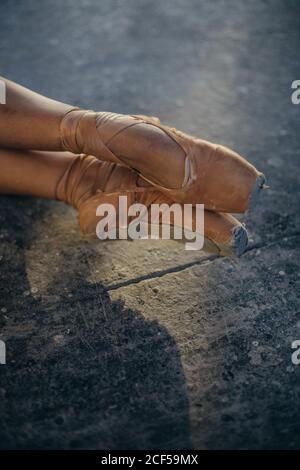 Dall'alto del ballerino femmina di raccolto in usurato fuori scarpe pointe che mantengono le gambe dritte sul pavimento grigio durante l'allenamento difficile in studio Foto Stock