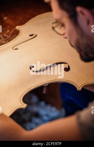 Vista laterale ad alto angolo del prodotto taglio di finitura artigianale attento f fori nella tavola da pranzo in legno per violino al tavolo in sala di lavoro Foto Stock