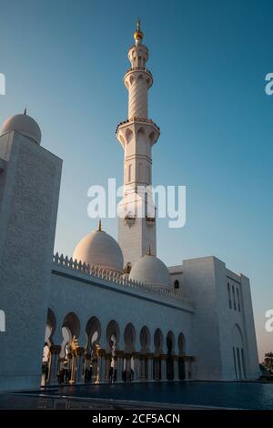 Incredibile enorme moschea con alta torre vicino alla piscina e cielo blu ad Abu Dhabi, Emirati Arabi Uniti Foto Stock