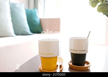 Tazze in ceramica con caffè fresco posto sul tavolo vicino al divano in un accogliente soggiorno a casa Foto Stock