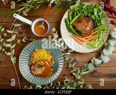 Gamba di lampada fritta imbottita e imbottita servita sui piatti con verdure fresche e riso tra ramoscelli verdi su legno tabella Foto Stock