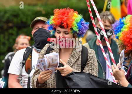 Un manifestante vestito da clown tiene falsi banconote durante la dimostrazione.all'esterno degli edifici del Tesoro dell'HM i manifestanti al carnevale della ribellione dell'estinzione della corruzione marciarono verso Buckingham Palace ma furono bloccati dalla polizia al Mall. Gli attivisti chiedono che coloro che sono al potere intraprendano azioni in materia di clima e ambiente. Foto Stock