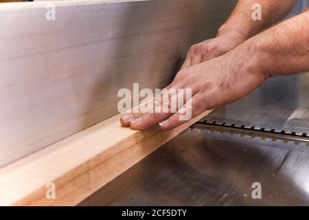 Uomo di legno in vestiti casual mettendo a fuoco e tagliando legname usando macchina elettrica speciale mentre si lavora in un'officina leggera e moderna Foto Stock