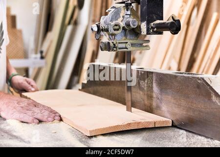 Uomo di legno in vestiti casual mettendo a fuoco e tagliando legname usando macchina elettrica speciale mentre si lavora in un'officina leggera e moderna Foto Stock