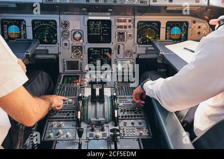 Vista posteriore di raccolto anonimo uomo capitano e pilota seduto in cabina di pilotaggio di aeroplano moderno e controllo delle attrezzature durante la preparazione per la partenza Foto Stock